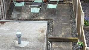 Un patio con pared de ladrillo, valla de madera y suelo de concreto.