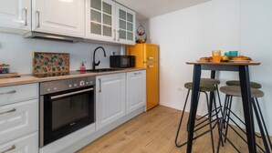 Eine Küche mit weißen Schränken, einer schwarzen Mikrowelle, einem gelben Kühlschrank und einem Barhocker.