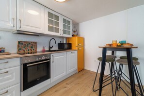 A kitchen with white cabinets, a black microwave, a yellow refrigerator, and a bar stool. - Traditional stone house w terrace, near the beach (Trogir)