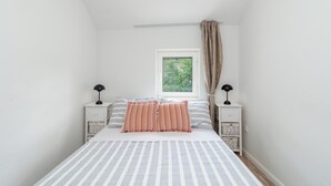 Ein Schlafzimmer mit einem Bett, zwei Nachttischen, einem Fenster und Blick ins Grüne.