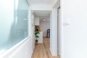 Un couloir étroit avec un mur blanc, un plancher en bois et une fenêtre sur le côté gauche.