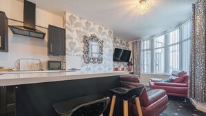Eine moderne Küche mit Flachbildfernseher, Mikrowelle und Kaffeemaschine. Zwei Barhocker und ein rotes Ledersofa sind ebenfalls vorhanden.