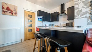 Eine kleine Küche mit einer Holztür, schwarzen Schränken, einer weißen Arbeitsplatte und einem roten Ledersessel.