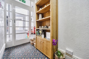 Eine Hotelhalle mit gemustertem Teppich, einem Holzschrank mit Dekoration, einem Feuerlöscher und einem Hinweis auf freie Zimmer.