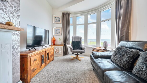 Ett vardagsrum med en stor platt-TV, en lädersoffa, ett träskåp och ett fönster med gardiner.