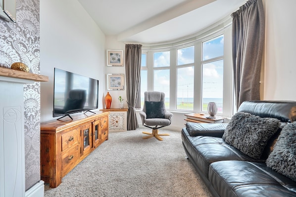 Ein Wohnzimmer mit einem großen Flachbildfernseher, einem Ledersofa, einem Holzschrank und einem fenster mit Vorhängen.
