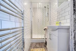 Ein modernes Badezimmer mit weißen Fliesen, einer Glasdusche, einem weißen Waschbecken mit gelbem Seifenspender und Holzboden.