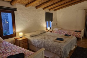 Een slaapkamer met twee bedden, een houten plafond, een raam en een nachtkastje met een lamp.