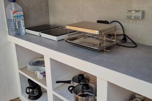 Een kitchenette met een waterdispenser, een broodrooster, een koffiezetapparaat en een pan op het aanrecht.