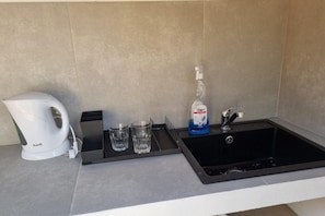 Een kitchenette met een koffiezetapparaat, twee glazen, een fles afwasmiddel en een spoelbak.