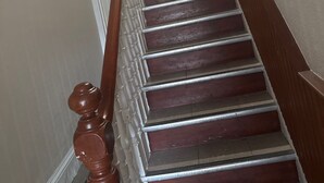 Un escalier en bois, doté d’une rampe, mène à un palier où est affichée une annonce encadrée.