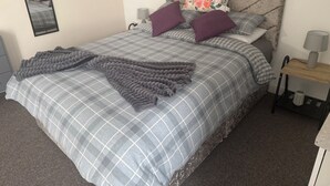 Un lit bien fait, recouvert d’une couvre-lit à carreaux, avec deux oreillers, un coussin décoratif, une lampe de chevet et une table de chevet également dotée d’une lampe.