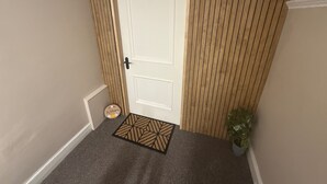 Une porte ornée d’un paillasson aux motifs géométriques, d’une petite pancarte de bienvenue et d’une plante en pot.