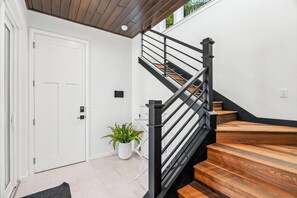 Eine Treppe mit schwarzen Geländern und Holzbodenstufen, eine weiße Tür und ein Blumentopf.