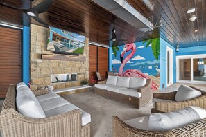 Eine Sitzecke mit Korbmöbeln, einer Steinwand, einem an der Wand befestigten Fernseher und einem Wandbild einer Flamingos.