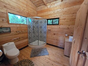 Et badeværelse i en træhytte med toilet, brusebad og vask.