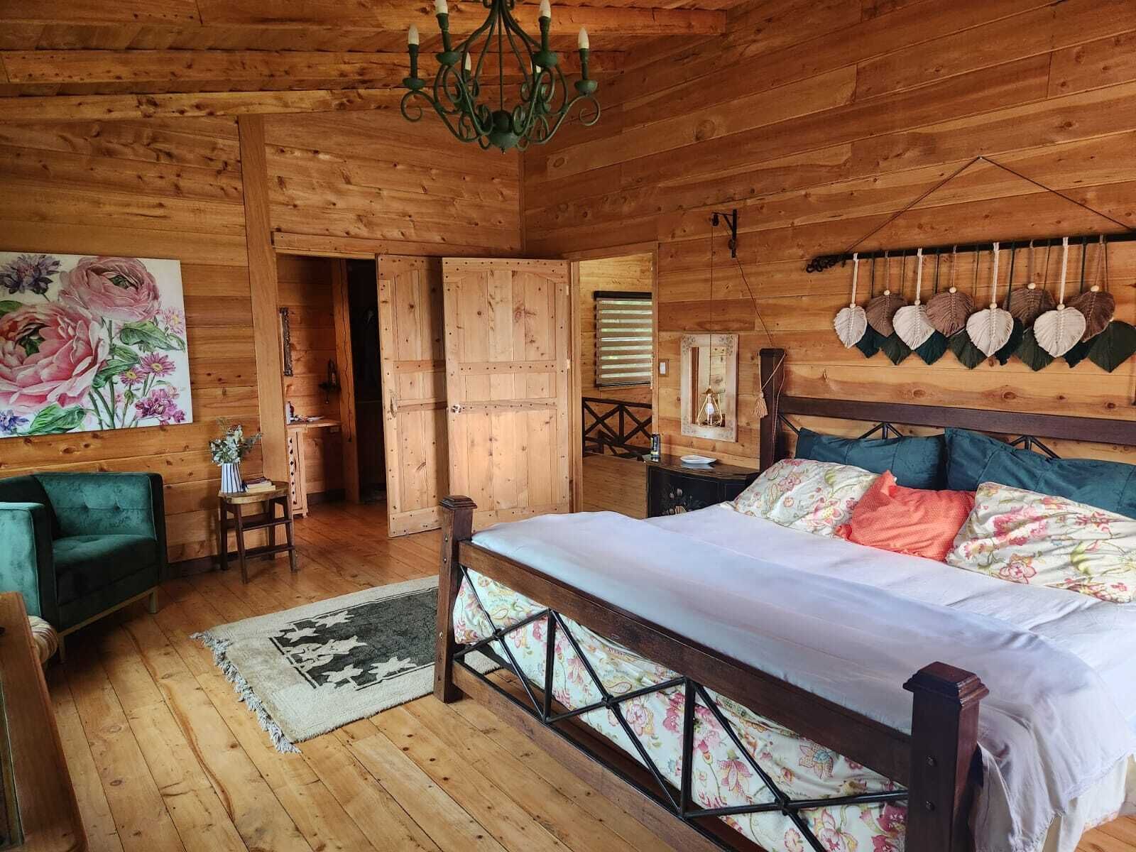 A wooden room with a bed, a green armchair, a chandelier, and a floral painting.