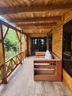 A wooden cabin with a porch, wooden benches, and a view of the surrounding forest.