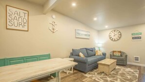 A living room with a blue sofa, a wooden bench, a clock, and a sign that says 'SALT AND SURF'.