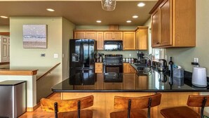 Una cocina con armarios de madera, un refrigerador negro, un microondas y una isla grande con taburetes de bar.