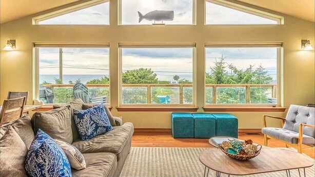 Una habitación espaciosa con techo alto, ventanas amplias, un sofá, una silla y una mesita.