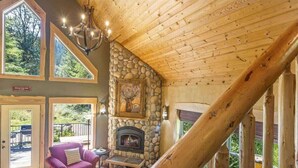 L’intérieur d’une cabane en rondins, avec une cheminée en pierre, de grandes fenêtres et un escalier en bois.