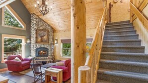 L’intérieur d’une cabane en rondins, avec une cheminée en pierre, un escalier et un coin salon confortable.