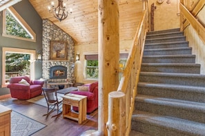 A log cabin interior with a stone fireplace, a staircase, and a cozy seating area.