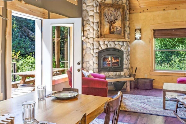 A cozy room with a stone fireplace, a wooden dining table, and a red sofa.