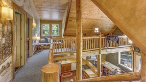 Une cabane en bois à plusieurs niveaux, comprenant une chambre à coucher en mezzanine, un coin repas et une cuisine.