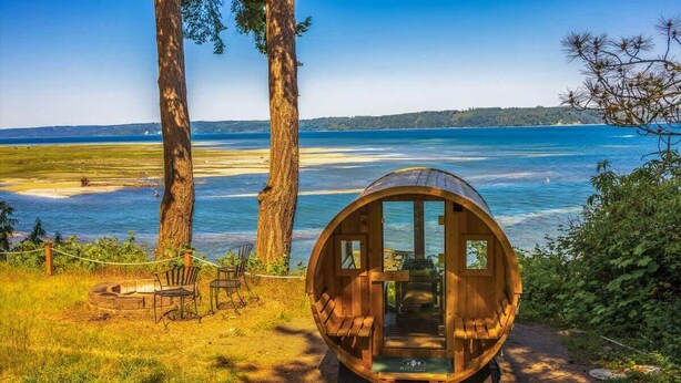 Une cabane en bois à la forme circulaire, située dans une zone herbeuse et offrant une vue sur un lac et des arbres.