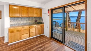Une cuisine avec des meubles en bois, un pare-feu en carrelage et une vue sur une terrasse dotée d’une rambarde et bordée d’arbres.