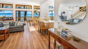Un vaste salon doté d’une grande fenêtre donnant sur la mer, un coin repas avec des meubles en bois et un miroir rond accroché au mur.
