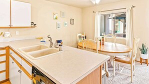 A kitchen with a double sink, wooden cabinets, a dishwasher, a dining table with chairs, and a window with curtains. - Walk to Downtown | Family-Friendly Condo | Dogs OK (Leavenworth)