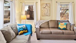 A living room with a sofa, a chair, a lamp, and a large window with curtains. - Walk to Downtown | Family-Friendly Condo | Dogs OK (Leavenworth)