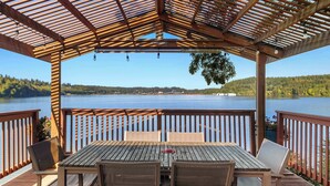 A covered outdoor seating area with a view of a lake and forest. - Waterfront Haven: Beach Access, Hot Tub, Fire Pit (Shelton)