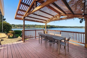 A wooden deck with a pergola, a table with chairs, and a view of a lake. - Waterfront Haven: Beach Access, Hot Tub, Fire Pit (Shelton)