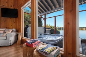 A cozy room with a sofa, a small table, a hot tub, and a view of a lake. - Waterfront Haven: Beach Access, Hot Tub, Fire Pit (Shelton)