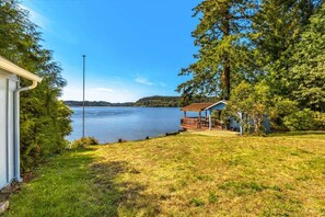 A lakeside property with a covered deck, a small shed, and a grassy area.