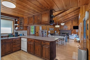 A spacious kitchen with wooden cabinets, a central island, and a dining area with a fireplace. - Waterfront Haven: Beach Access, Hot Tub, Fire Pit (Shelton)
