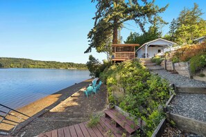 A lakeside property with a wooden deck, chairs, and a covered area with a table. - Waterfront Haven: Beach Access, Hot Tub, Fire Pit (Shelton)