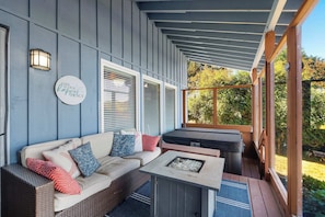 A covered porch with a sofa, cushions, and a fire pit.