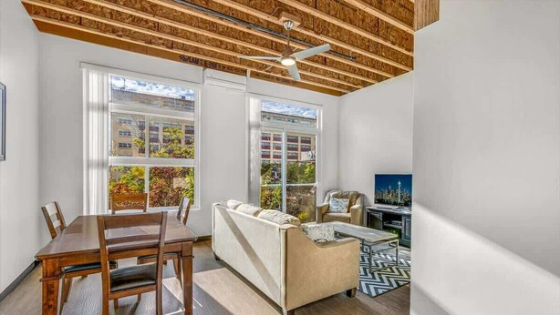 A modern living room with a dining area, large windows, and a ceiling fan.