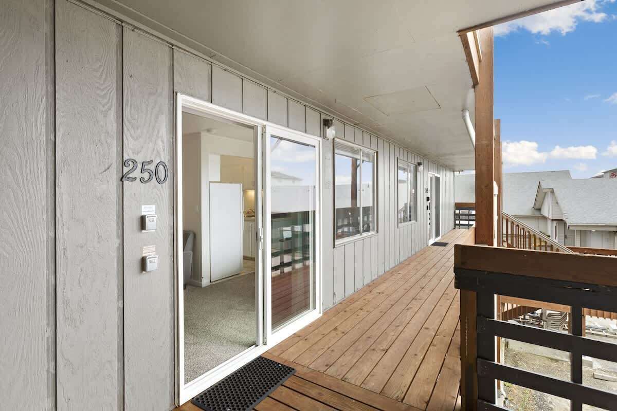 A covered outdoor area with a wooden deck, sliding glass doors, and a view of a residential neighborhood.