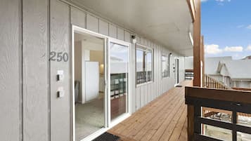 A covered outdoor area with a wooden deck, sliding glass doors, and a view of a residential neighborhood.