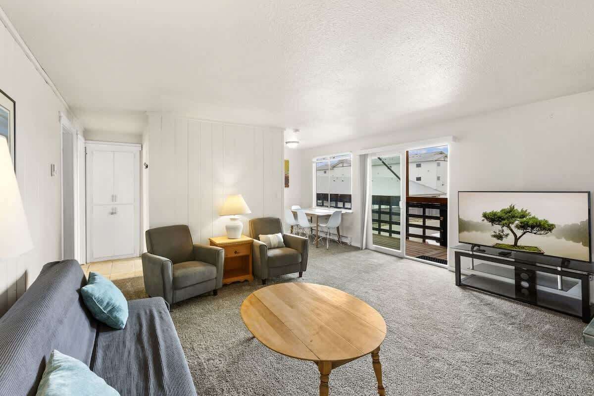 A modern living room with a sofa, chairs, a coffee table, a TV, and a sliding glass door leading to a balcony.
