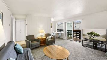 A modern living room with a sofa, chairs, a coffee table, a TV, and a sliding glass door leading to a balcony.