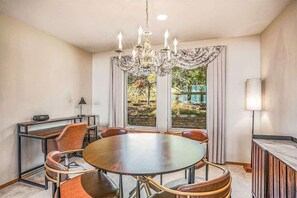 Een eetgedeelte met een ronde tafel, stoelen, een kroonluchter en een uitzicht door grote ramen.