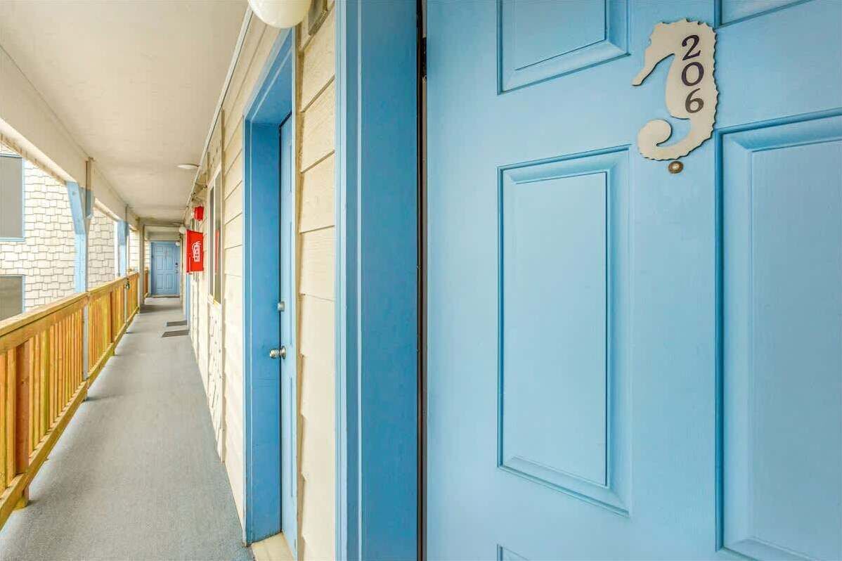 Un pasillo con puertas azules, barandilla de madera y un letrero rojo.