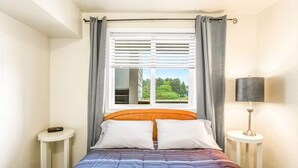 A bedroom with a bed, a window with curtains, a bedside table, and a lamp. - 1BR Condo | Dogs OK | Close to Ocean & Town (Ocean Shores)